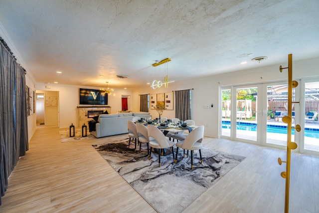 dining area featuring a notable chandelier, light hardwood / wood-style flooring, french doors, a textured ceiling, and crown molding