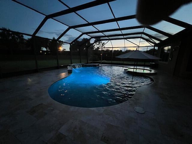 pool at dusk featuring an in ground hot tub, a patio, and glass enclosure