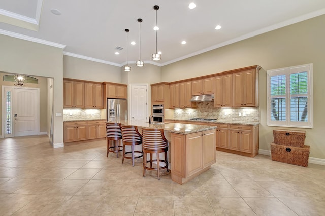 kitchen with light stone counters, crown molding, a center island with sink, appliances with stainless steel finishes, and a towering ceiling