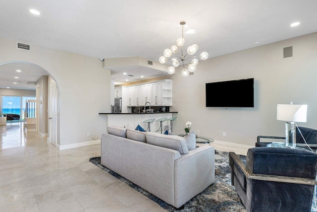 living room featuring a textured ceiling, an inviting chandelier, and sink