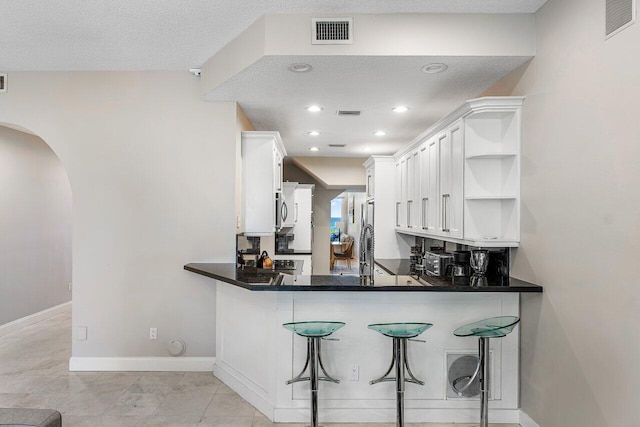 kitchen featuring a breakfast bar area, kitchen peninsula, white cabinetry, and a textured ceiling