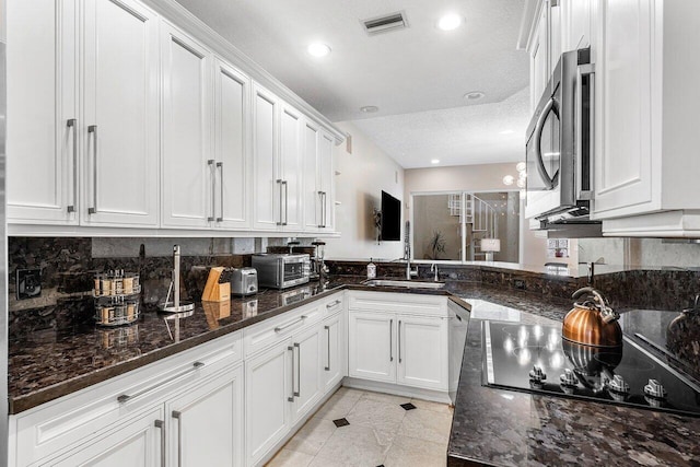 kitchen with kitchen peninsula, dark stone counters, a textured ceiling, stainless steel appliances, and white cabinets