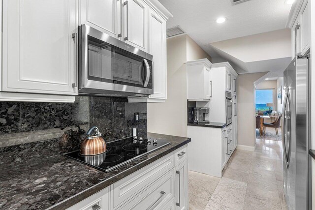 kitchen with stainless steel appliances, white cabinetry, tasteful backsplash, and dark stone counters