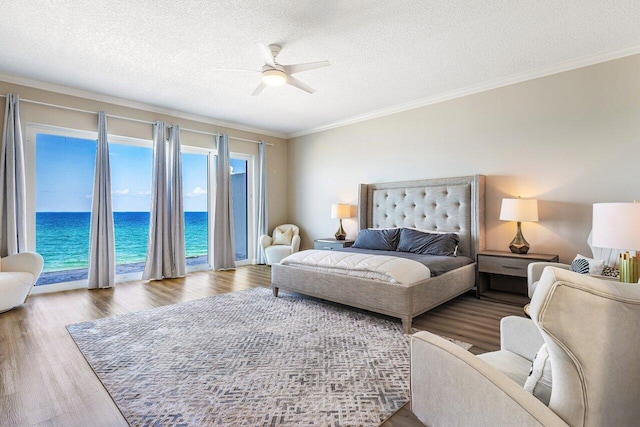 bedroom featuring a textured ceiling, crown molding, a water view, and wood-type flooring