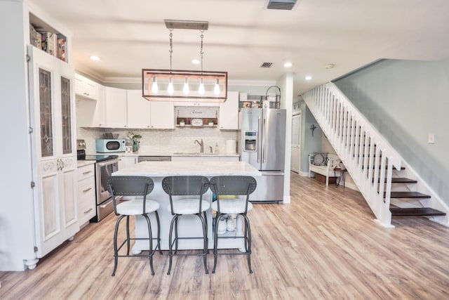 kitchen with a breakfast bar, light wood-style flooring, appliances with stainless steel finishes, white cabinets, and a sink