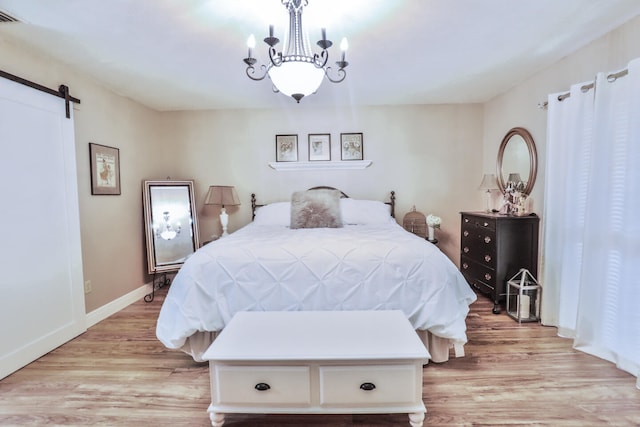 bedroom featuring a notable chandelier, light hardwood / wood-style flooring, and a barn door