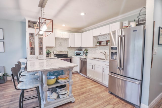 kitchen featuring stainless steel appliances, light hardwood / wood-style floors, white cabinetry, decorative backsplash, and sink