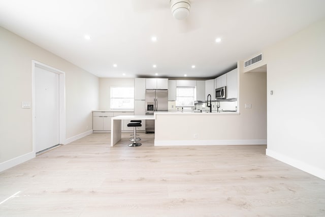 kitchen featuring a breakfast bar area, light hardwood / wood-style floors, a center island, sink, and white cabinets