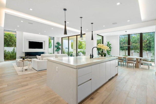 kitchen with white cabinets, hanging light fixtures, a center island with sink, and a healthy amount of sunlight