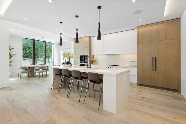 kitchen with decorative light fixtures, white cabinetry, an island with sink, light wood-type flooring, and a kitchen breakfast bar