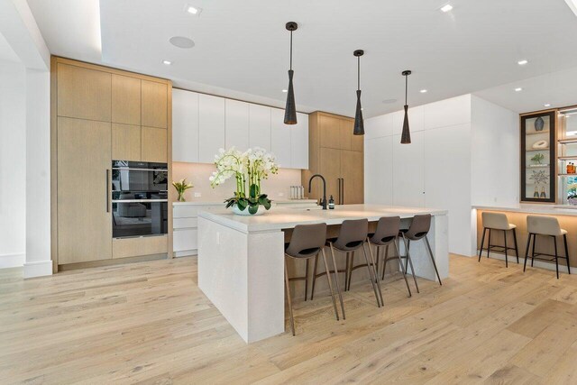 kitchen with light hardwood / wood-style flooring, a kitchen bar, black double oven, a center island with sink, and pendant lighting