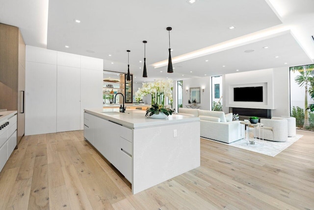 kitchen with decorative light fixtures, an island with sink, sink, white cabinets, and light hardwood / wood-style flooring