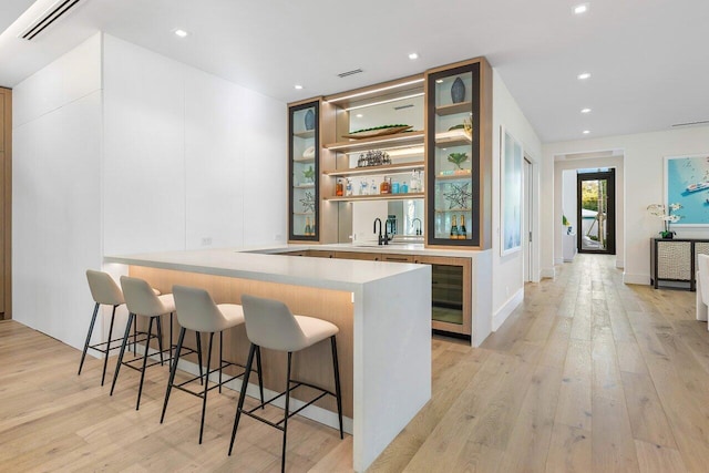 bar with sink, wine cooler, and light wood-type flooring