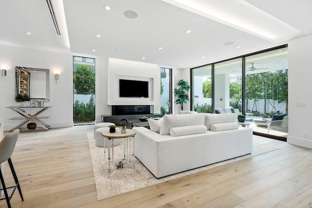 living room with ceiling fan, light hardwood / wood-style flooring, and a wall of windows