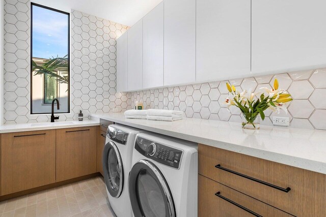 clothes washing area featuring light tile patterned floors, washing machine and dryer, sink, and cabinets