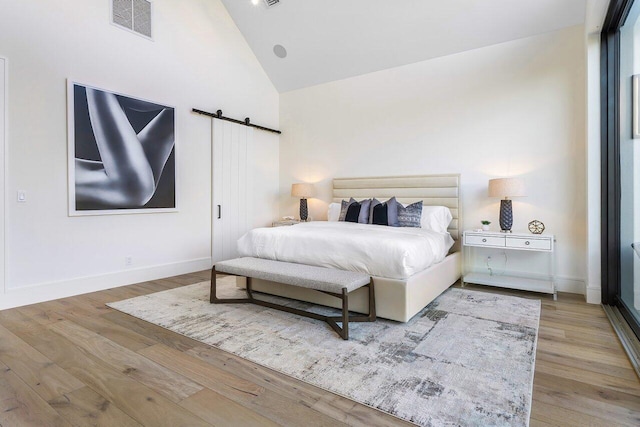 bedroom with light hardwood / wood-style flooring, high vaulted ceiling, and a barn door