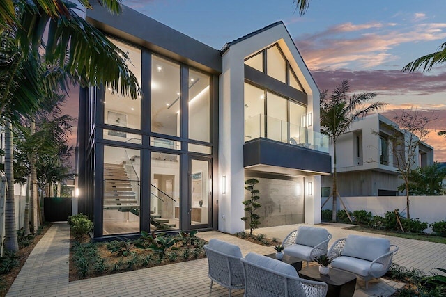 back house at dusk featuring a garage, outdoor lounge area, and a patio area