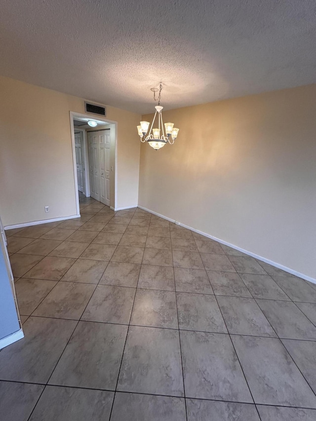 empty room featuring tile patterned floors, a textured ceiling, and an inviting chandelier