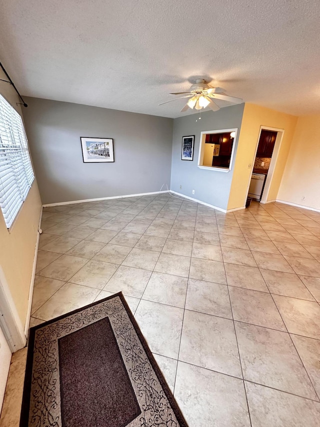 empty room featuring a textured ceiling, baseboards, a ceiling fan, and light tile patterned flooring