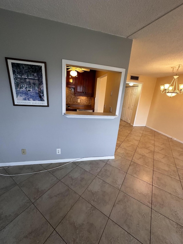 empty room featuring ceiling fan with notable chandelier, a textured ceiling, baseboards, and tile patterned floors