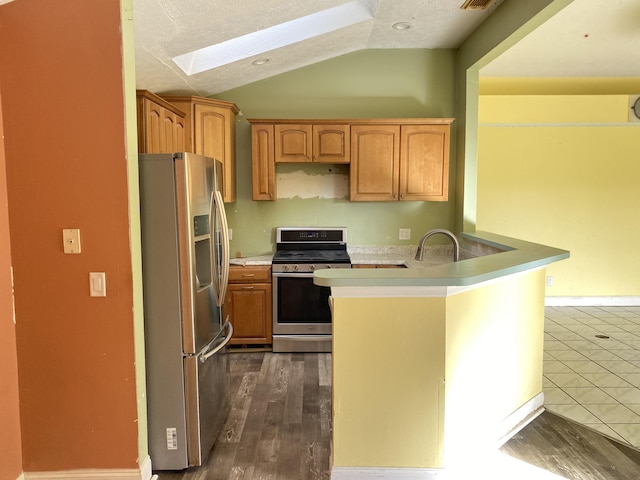 kitchen with appliances with stainless steel finishes, vaulted ceiling with skylight, a textured ceiling, dark hardwood / wood-style flooring, and kitchen peninsula