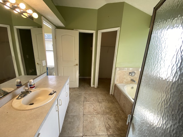 bathroom with lofted ceiling, vanity, tile patterned floors, and tiled bath