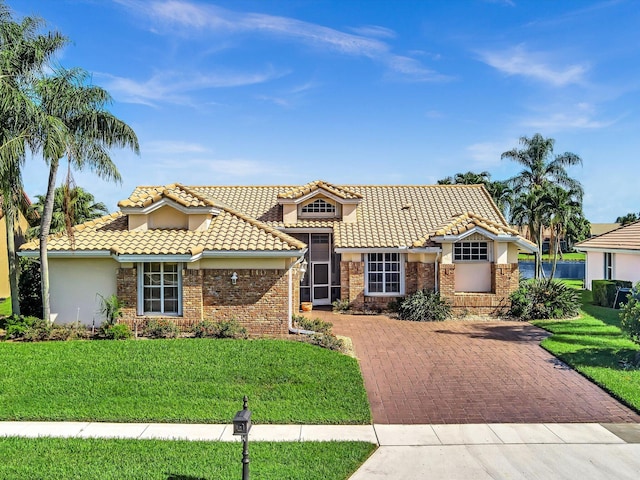 mediterranean / spanish-style house with brick siding, a tile roof, stucco siding, and a front yard