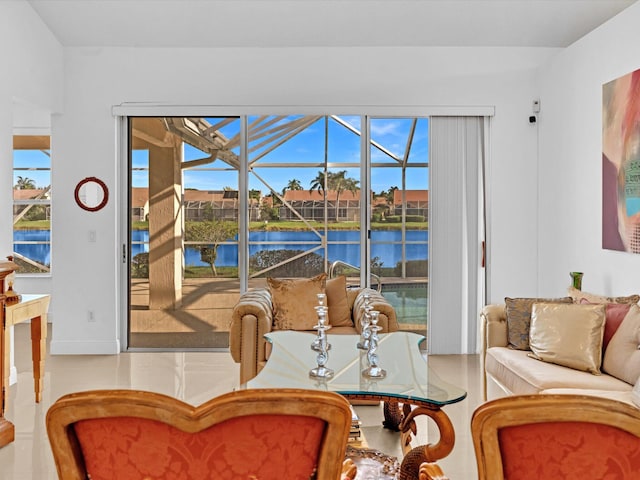 tiled living area with a sunroom, a water view, and baseboards