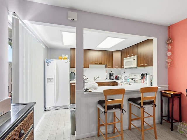 kitchen featuring a kitchen breakfast bar, kitchen peninsula, light hardwood / wood-style floors, and white appliances