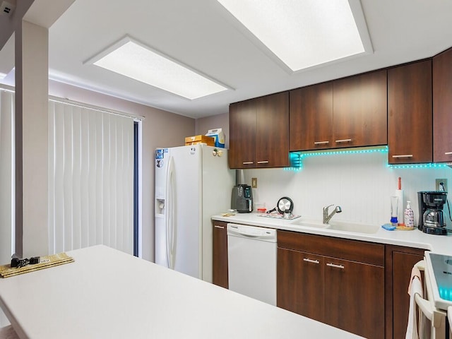 kitchen featuring white appliances, backsplash, sink, a skylight, and kitchen peninsula