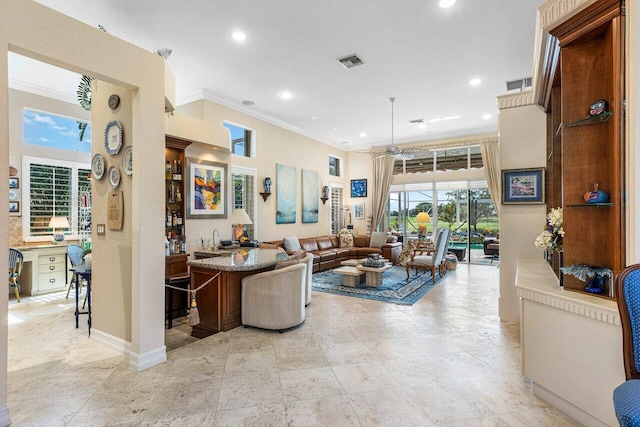 living room with ceiling fan, ornamental molding, and bar area