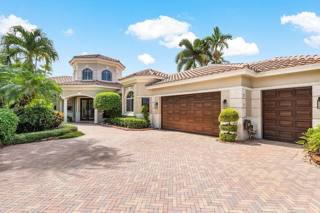 mediterranean / spanish house featuring decorative driveway, french doors, a garage, and stucco siding