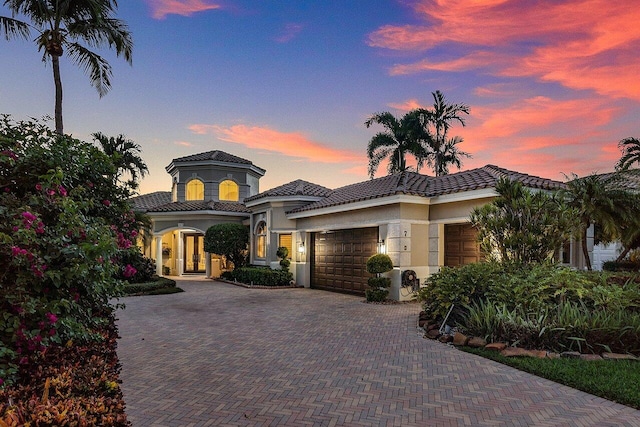 view of front of property with stucco siding, french doors, a garage, a tiled roof, and decorative driveway