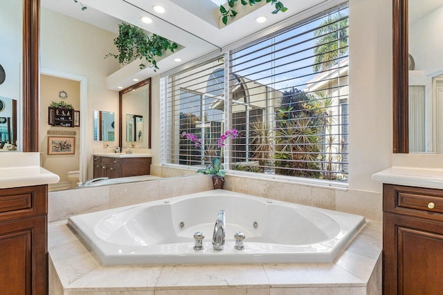 bathroom with vanity, tiled tub, and toilet