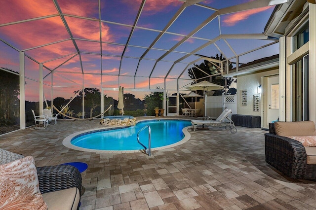 pool at dusk with glass enclosure and a patio area