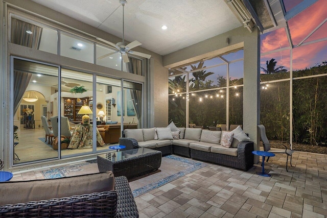 patio terrace at dusk featuring ceiling fan, an outdoor hangout area, and glass enclosure