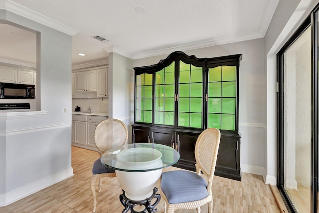 dining room featuring sink, light wood-type flooring, and ornamental molding