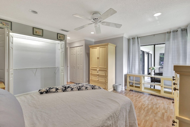 bedroom with light wood-type flooring, a textured ceiling, crown molding, multiple closets, and ceiling fan