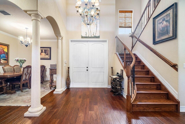 entryway with crown molding, an inviting chandelier, dark hardwood / wood-style floors, a high ceiling, and ornate columns