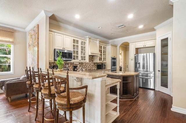 kitchen with a breakfast bar area, appliances with stainless steel finishes, a kitchen island, light stone countertops, and cream cabinetry