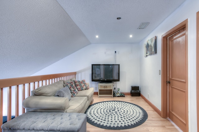 living room featuring a textured ceiling, lofted ceiling, and light hardwood / wood-style floors