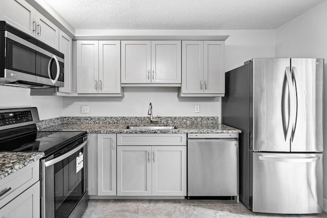 kitchen featuring dark stone countertops, a textured ceiling, stainless steel appliances, and a sink