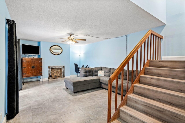 living area featuring a ceiling fan, a textured ceiling, baseboards, and stairs