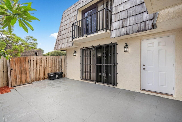 property entrance with a patio, mansard roof, a balcony, fence, and stucco siding