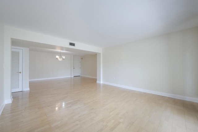 spare room with a notable chandelier and light hardwood / wood-style floors