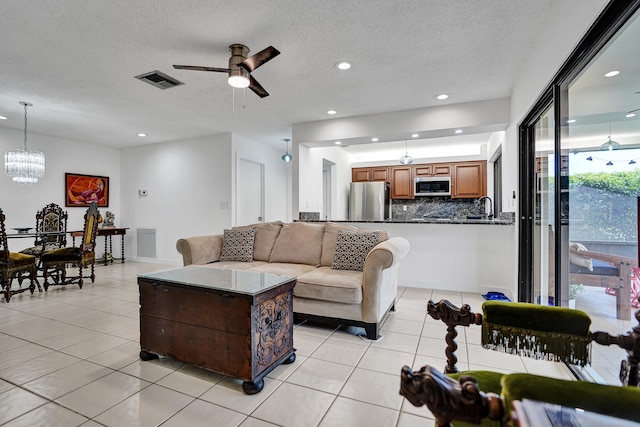 tiled living room with a textured ceiling, ceiling fan with notable chandelier, and sink