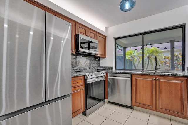 kitchen with appliances with stainless steel finishes, tasteful backsplash, sink, dark stone counters, and light tile patterned flooring