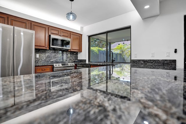 kitchen featuring dark stone counters, backsplash, sink, stainless steel appliances, and pendant lighting