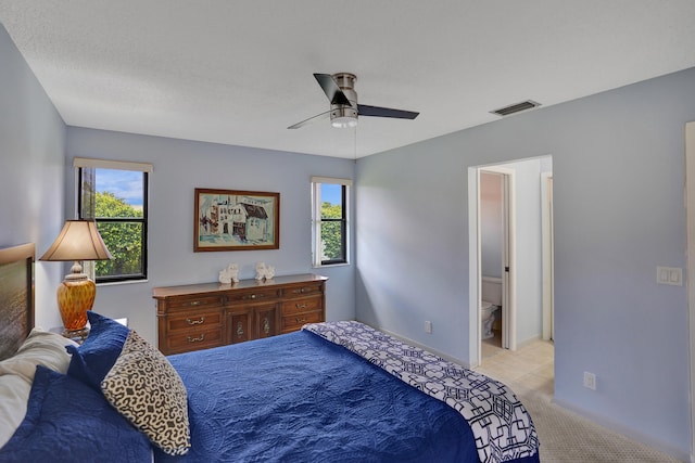 bedroom with multiple windows, light carpet, ensuite bathroom, and ceiling fan