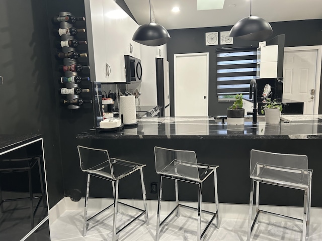 kitchen featuring dark stone counters, white cabinets, pendant lighting, and a kitchen breakfast bar